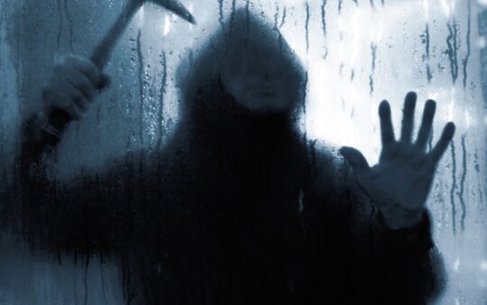 Einbrecher mit Hammer hinter Glasscheibe