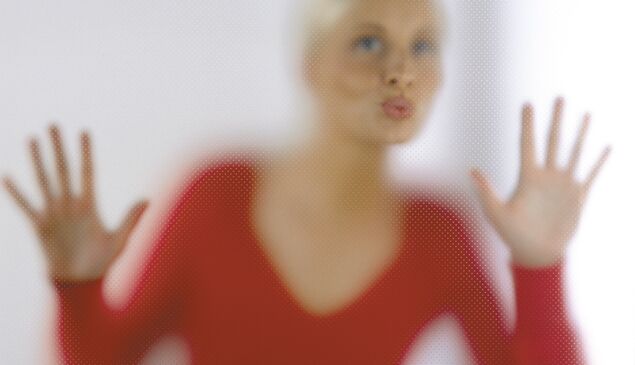 Frau in rotem Oberteil hinter gefrosteter Glasscheibe